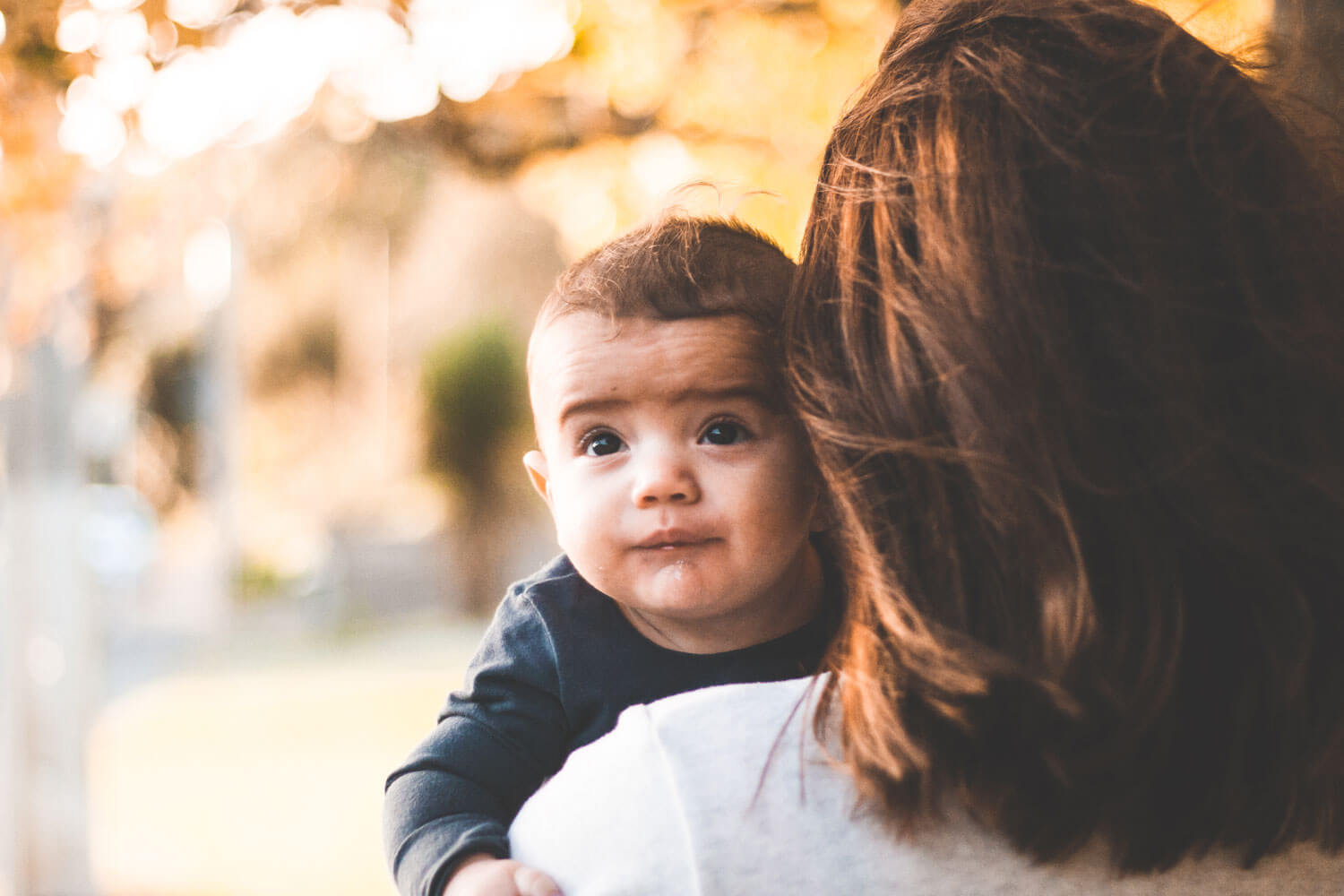 A young baby looks behind his mother's shoulder