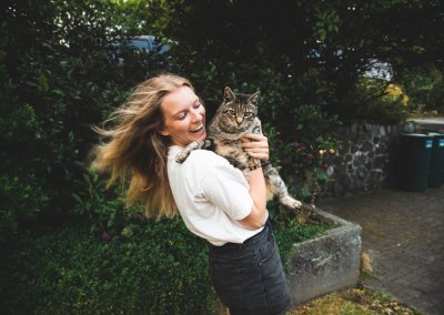 A young woman holding a cat with a backdrop of foliage