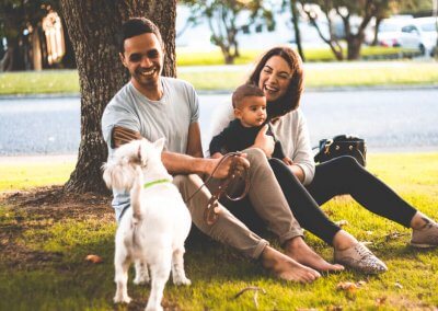 A small family sitting under a tree laughing at their dog